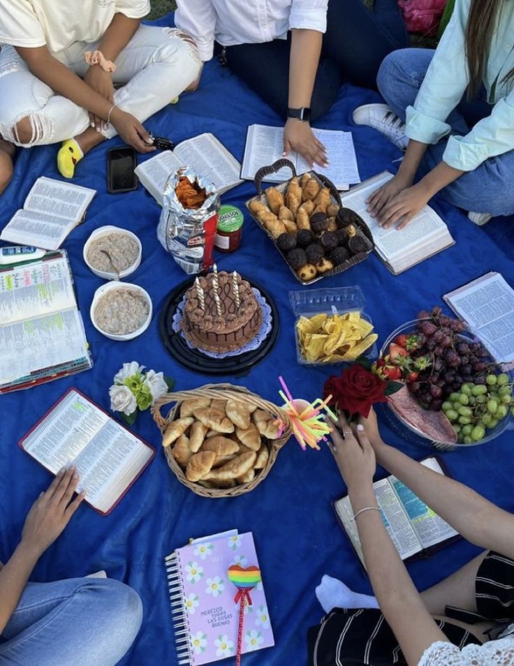 a group of people sitting around a blue table with food on it and open books