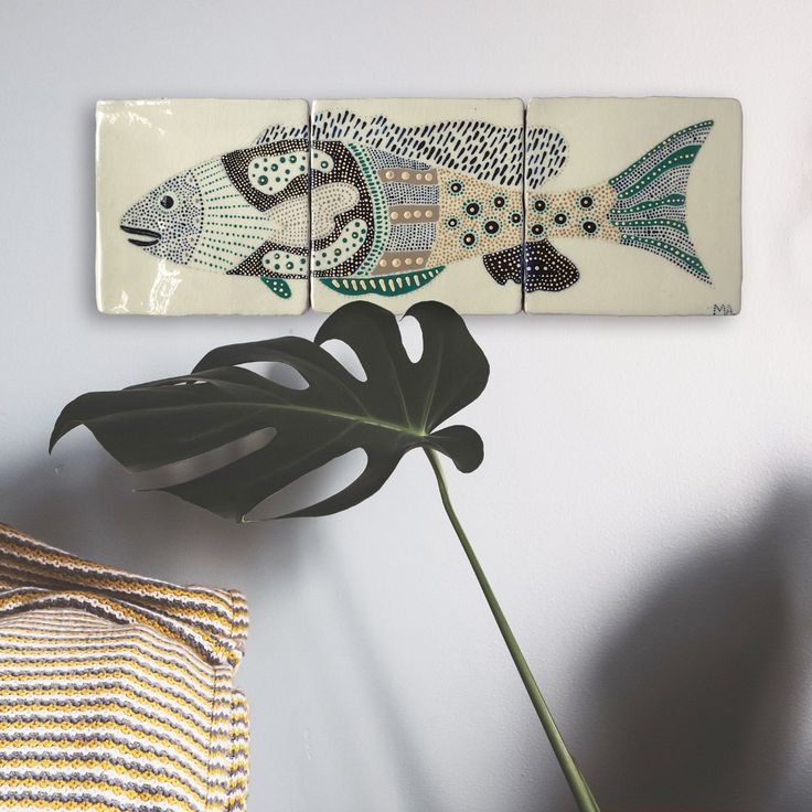 a wall hanging with fish on it next to a plant