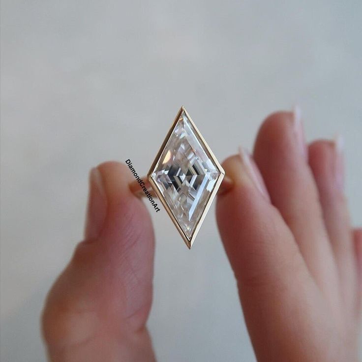 a person holding a ring in their left hand with a square shaped diamond on it