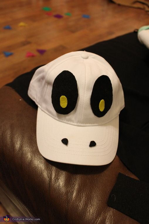 a white hat with black eyes is sitting on top of a brown leather chair in front of a wooden floor