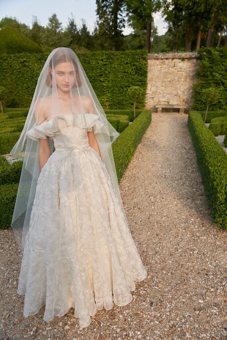 a woman wearing a wedding dress and veil standing in the middle of a gravel path