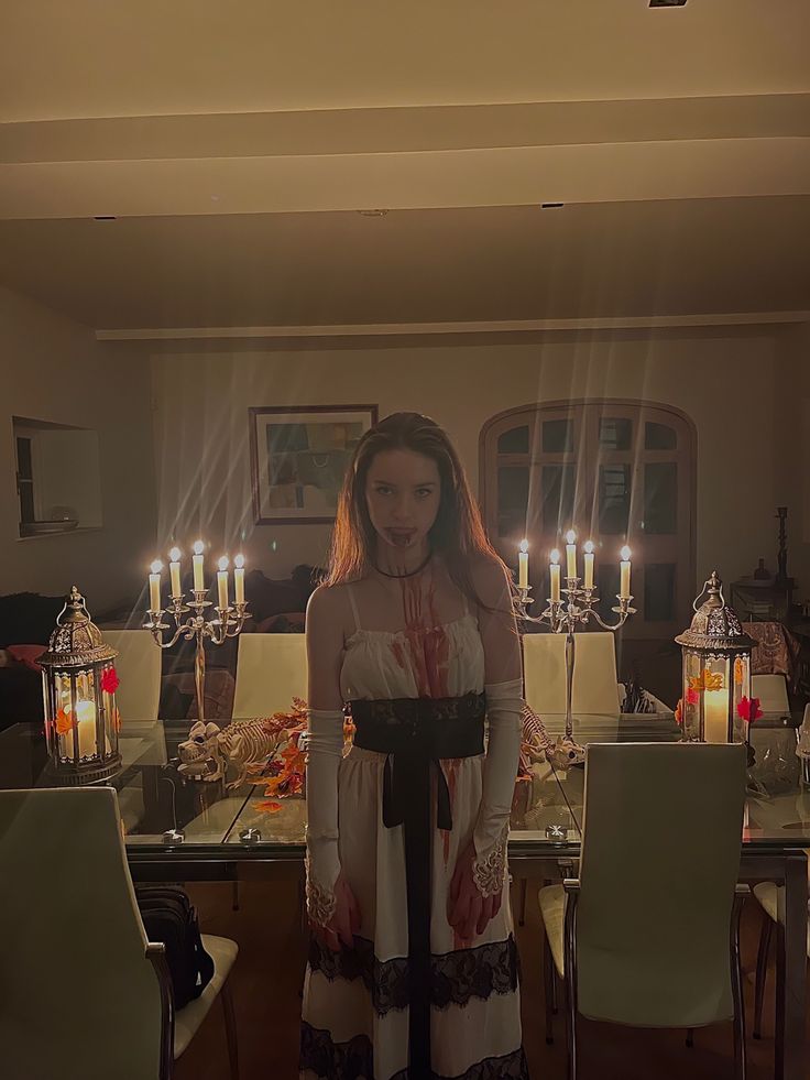 a woman standing in front of a dining room table with candles lit up behind her