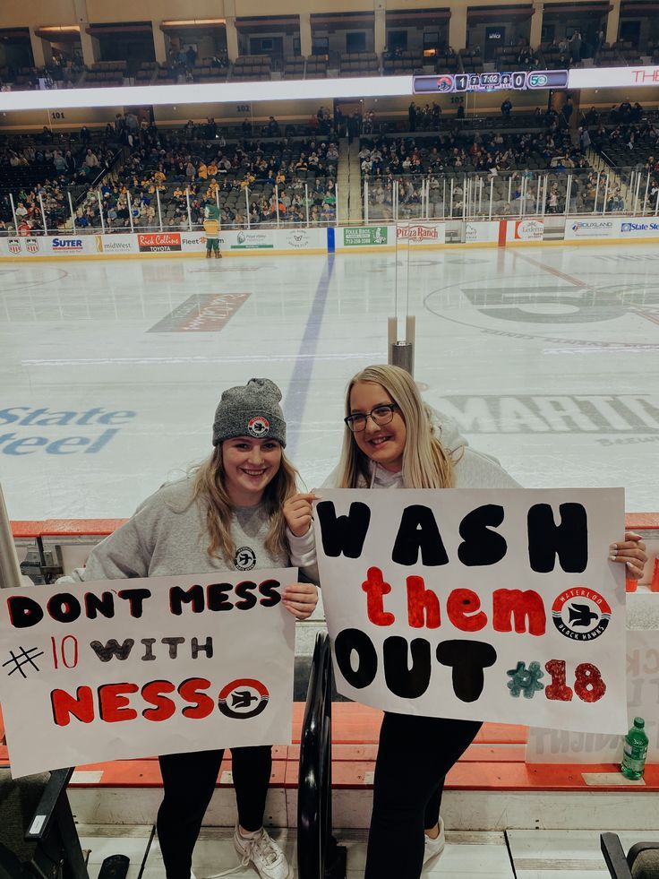 two women holding signs in front of an ice rink