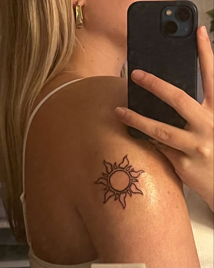 a woman with a sun tattoo on her arm holding a cell phone up to her face