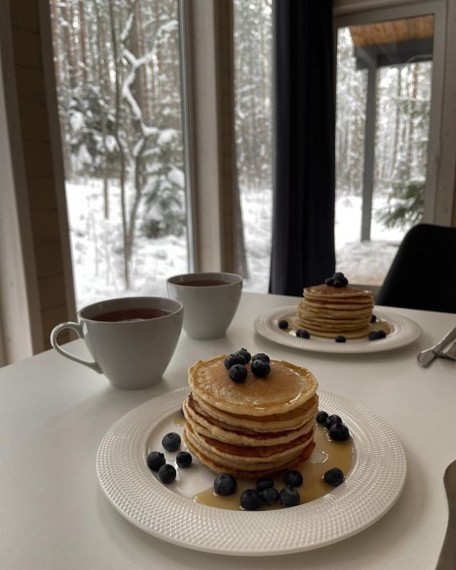 pancakes with blueberries and syrup on a white table in front of a snowy forest