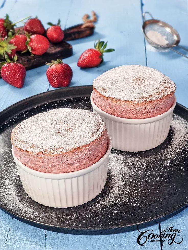 two desserts sitting on top of a black plate covered in powdered sugar next to strawberries