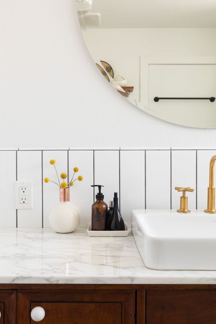 a bathroom with marble counter tops and gold faucets on the sink, along with a round mirror