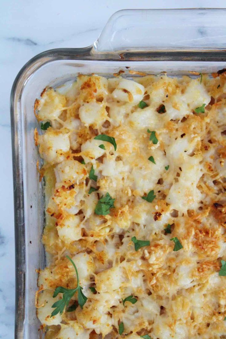 a casserole dish with cheese and parsley in it on a marble surface