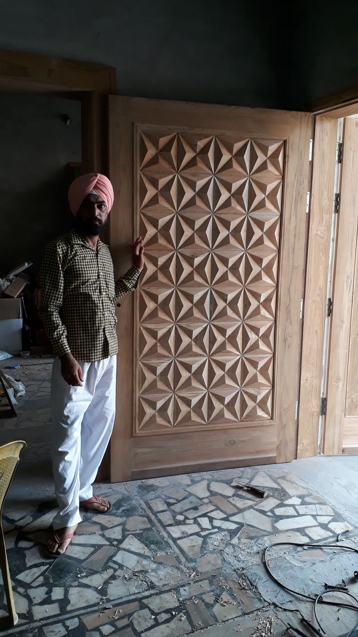 a man standing in front of a wooden door wearing a turban and white pants