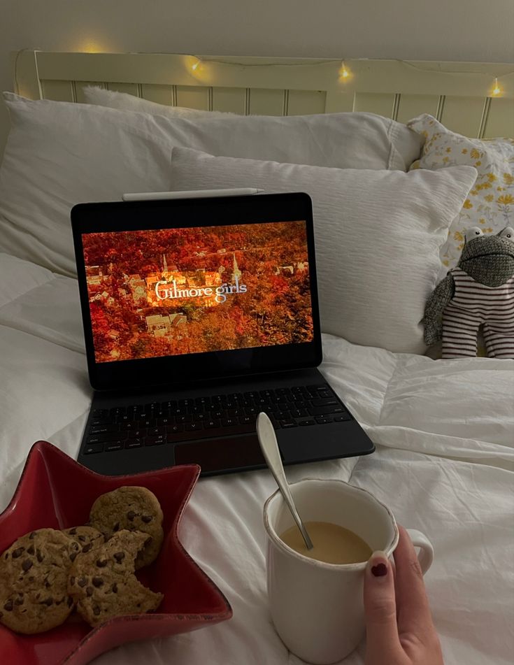 a laptop computer sitting on top of a bed next to a cup of coffee and cookies