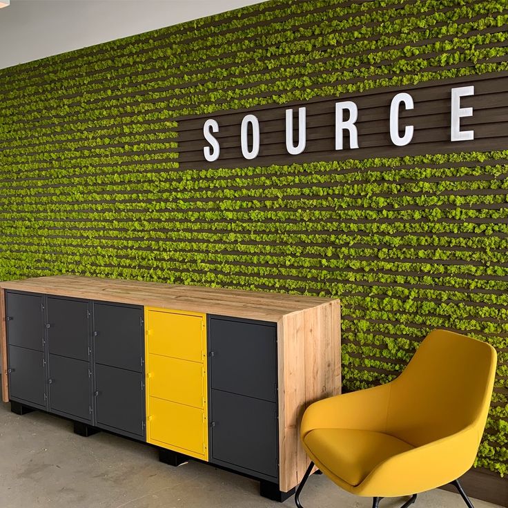 a yellow chair sitting in front of a wall covered with green plants and the word source on it