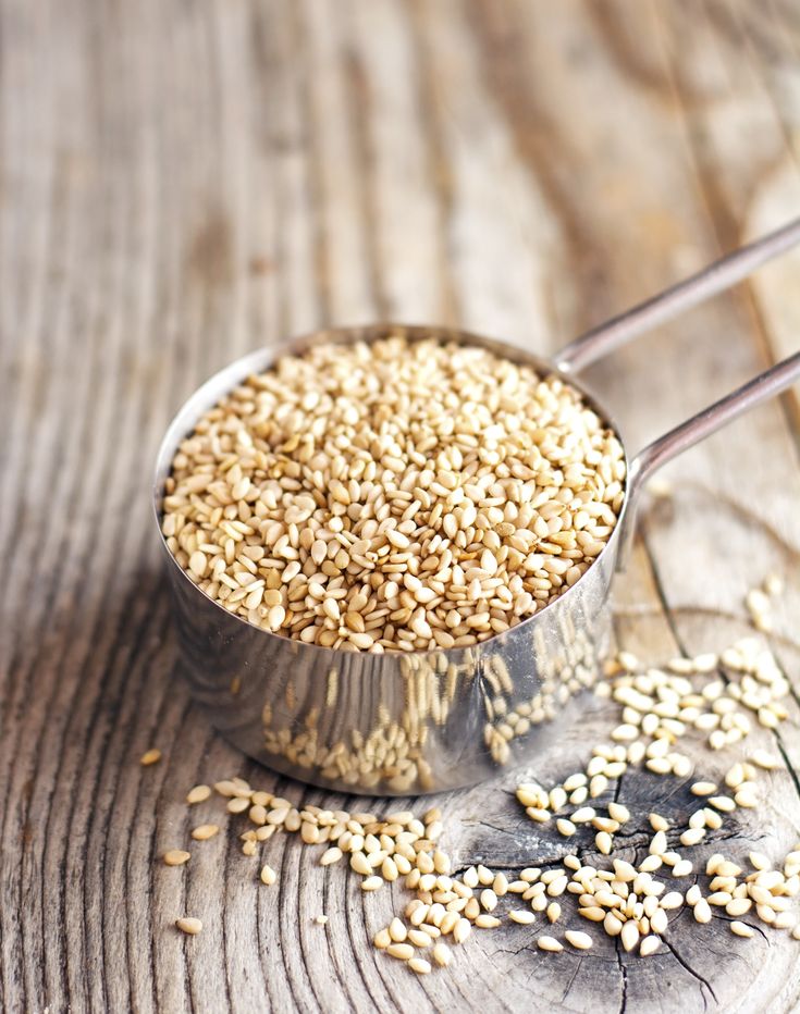 a spoon full of sesame seeds on top of a wooden table