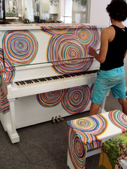 a man standing next to a white piano covered in multicolored swirls on it