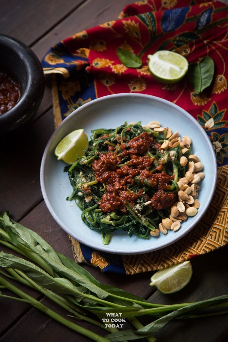 a white bowl filled with green beans and sauce on top of a wooden table next to lime wedges