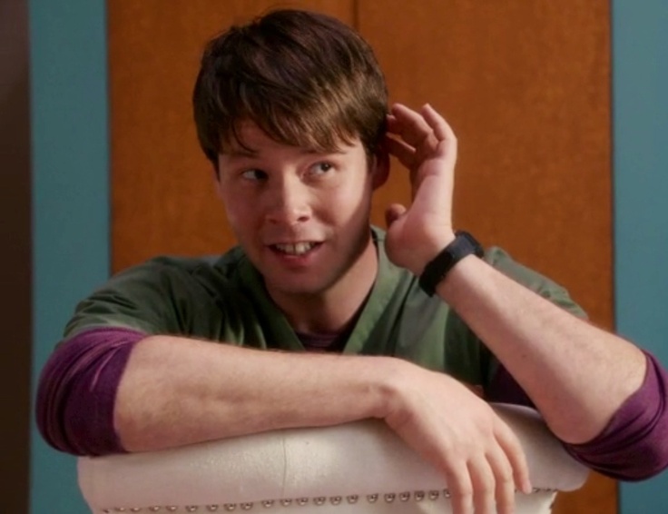 a young man sitting on top of a white chair with his hand on his head