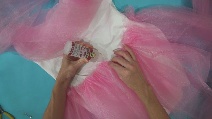 a woman in pink tulle skirt and white shirt using glue to make a dress