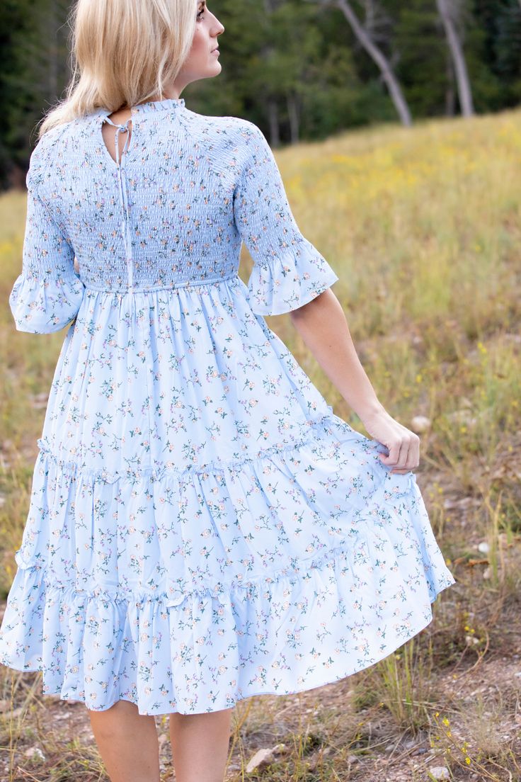 Ensure you remain the most stylish in any setting with the Dahlia Dress. Crafted with a soft-to-touch fabric, this baby blue dress features a darling floral pattern that will swoon you and passersby. Flared half sleeves and a high neckline make this a perfect transition piece when the temperature starts to dip in the evenings. STYLE INFO & CARE The smocked bodice for a flexible, comfortable fit Tiered Skirt Fully Lined 100% Polyester Hand washes in cold water, or for best results, dry clean. Siz Light Blue Midi Dress With Floral Embroidery, Casual Light Blue Floral Embroidered Dress, Blue Knee-length Ditsy Floral Dress, Light Blue A-line Midi Dress With Floral Print, Blue Floral Print Midi Dress With 3/4 Sleeve, Baby Blue Dresses, Tier Skirt, Floral Midi Dress, High Neckline