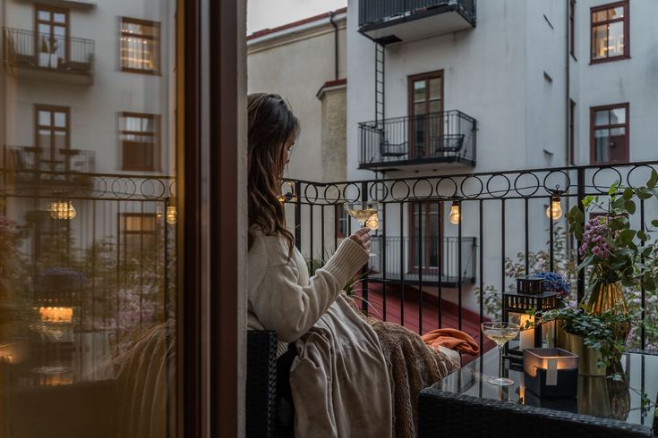 a woman standing on a balcony holding a wine glass in her hand and looking out the window