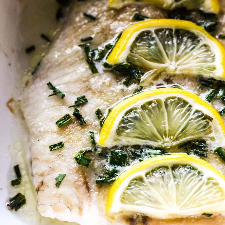 fish with lemons and herbs on it in a white casserole dish, ready to be eaten