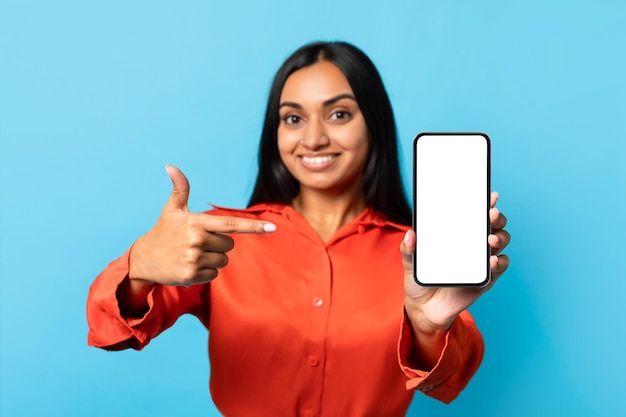 a woman in an orange shirt is holding up her cell phone and pointing at the screen