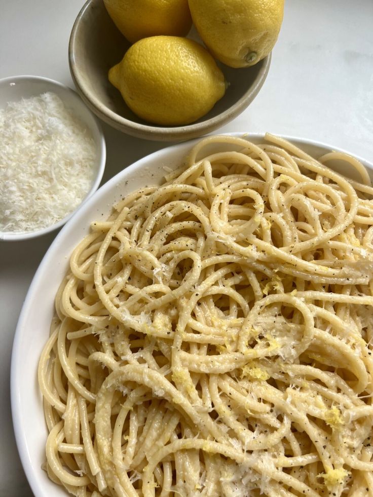 a plate of pasta with lemons and parmesan cheese next to it on a table