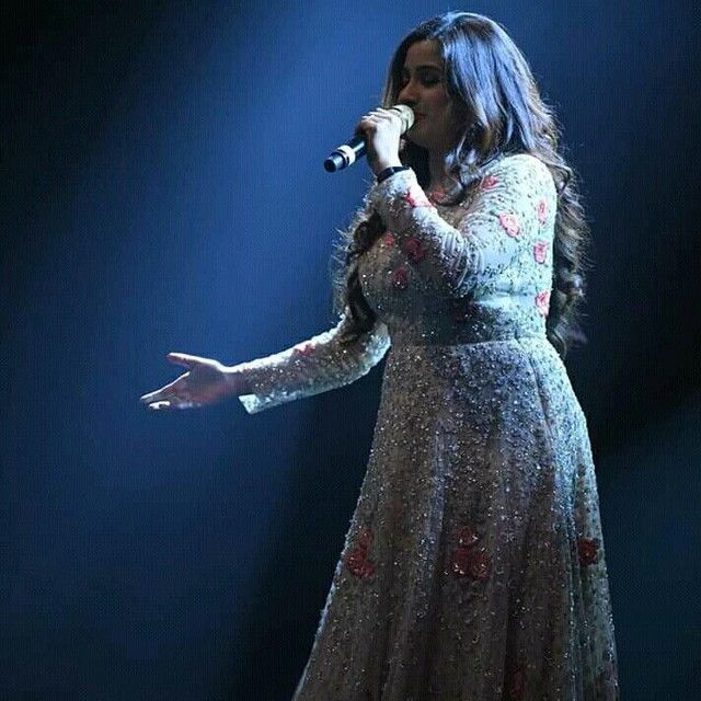 a woman in a long dress holding a microphone and singing into the air on stage