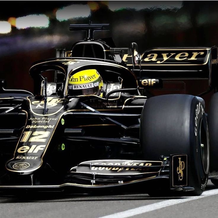 a black and gold race car driving down the road at night time with lights in the background