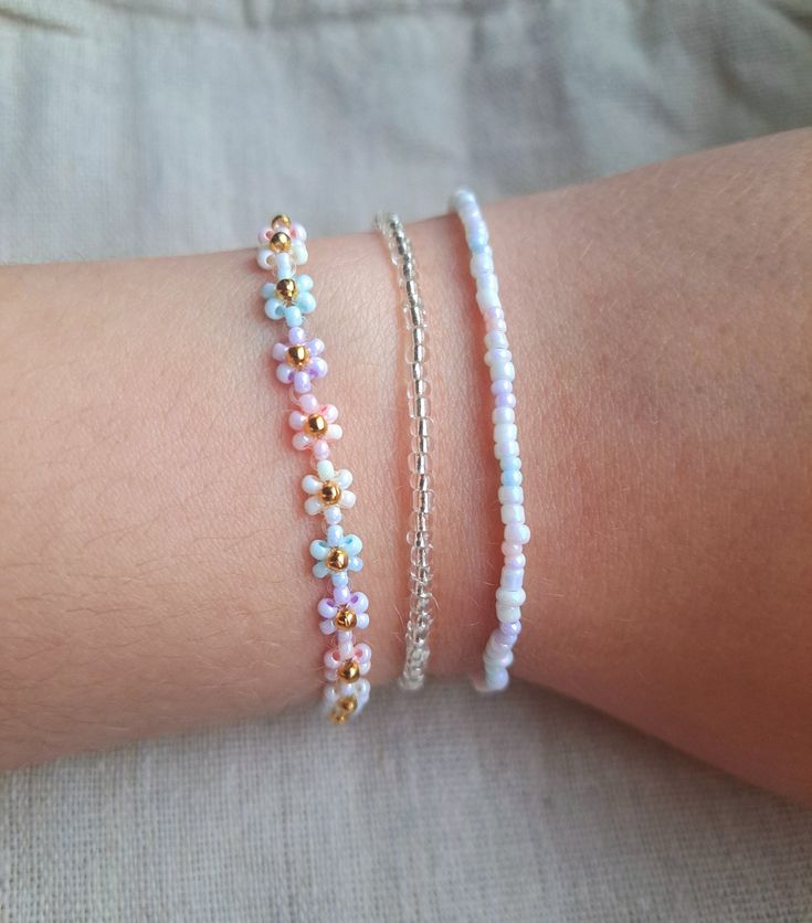 three different bracelets on someone's arm, one with beads and the other with flowers