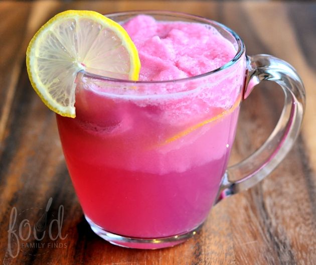 a glass mug filled with pink liquid and lemon wedged in it on top of a wooden table