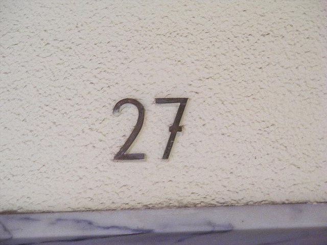 the number twenty seven is shown in black on a white stucco wall with a marble border