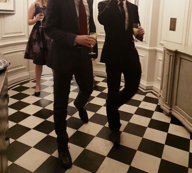 two men in suits and ties standing on a black and white checkerboard floor