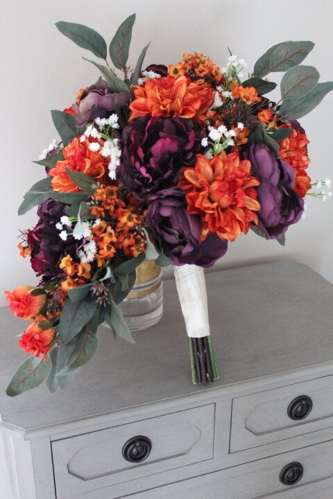 a bouquet of flowers sitting on top of a dresser next to a vase filled with orange and purple flowers