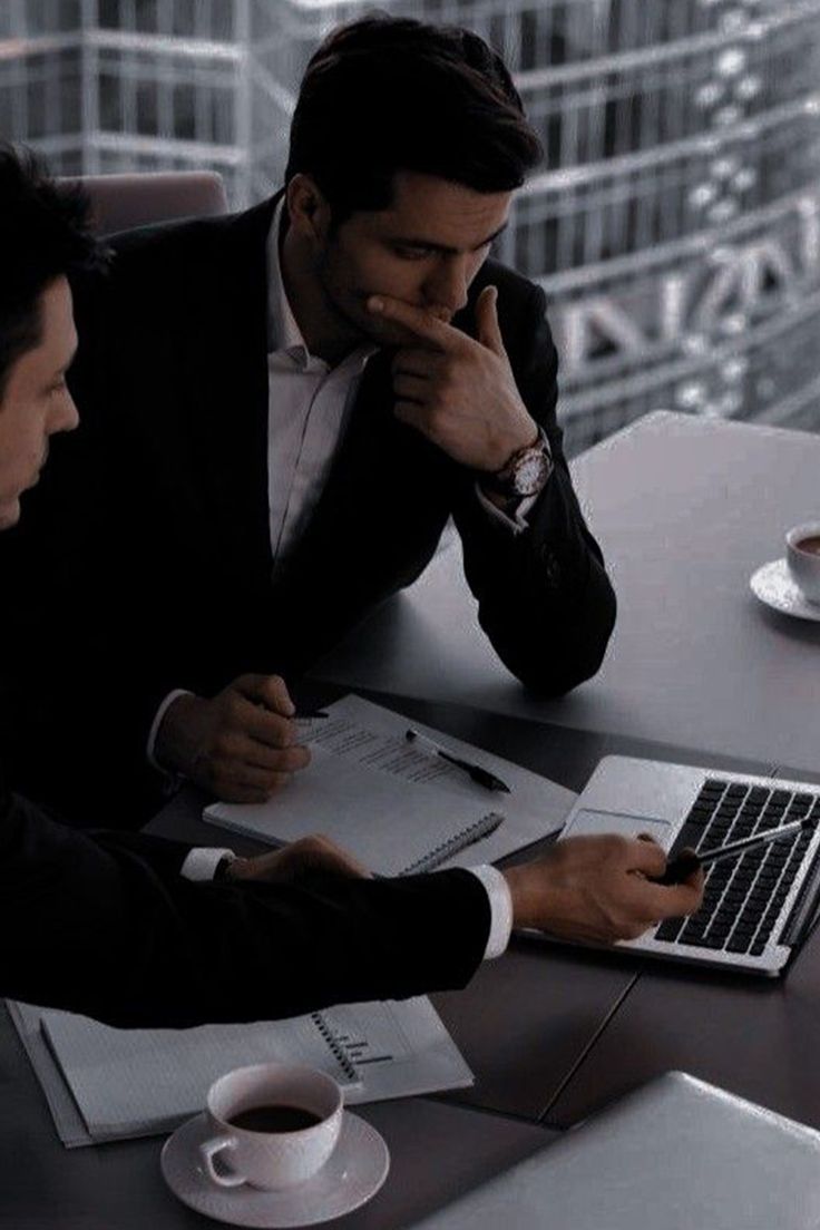 two men sitting at a table with laptops and papers in front of their faces