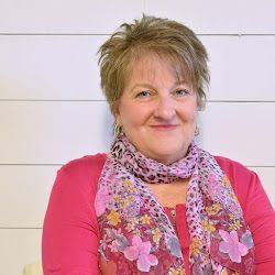 a woman wearing a pink shirt and scarf with flowers on it, standing in front of a white wall