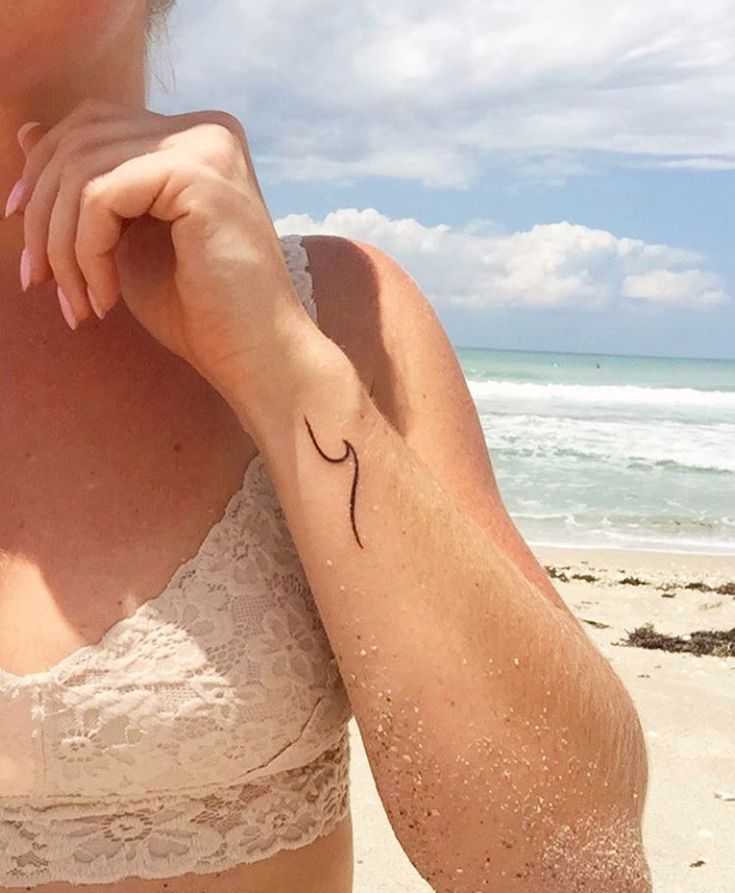 a woman with a small tattoo on her arm standing in the sand at the beach