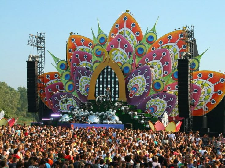 a large group of people standing in front of a stage with an elaborately designed peacock on it