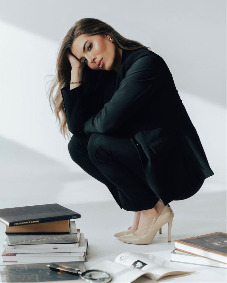 a woman kneeling down with her hand on her face next to some books and a pair of high heels