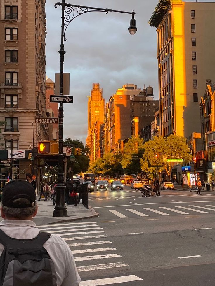 a man is walking across the street in front of tall buildings and traffic lights at sunset