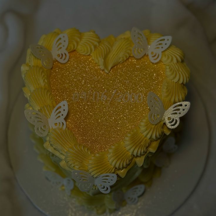 a heart shaped cake with yellow frosting and white butterflies on the top, sitting on a plate