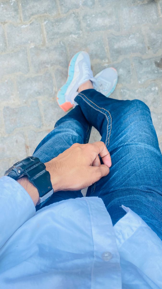 a person sitting on the ground with their foot in his jeans and wearing a watch