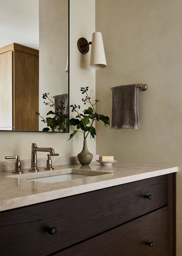 a bathroom sink with a vase on top of it next to a mirror and lights