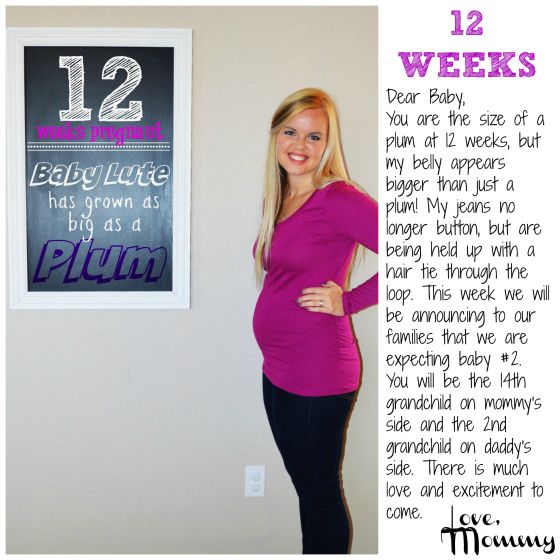 a pregnant woman standing in front of a sign with the words 12 weeks written on it