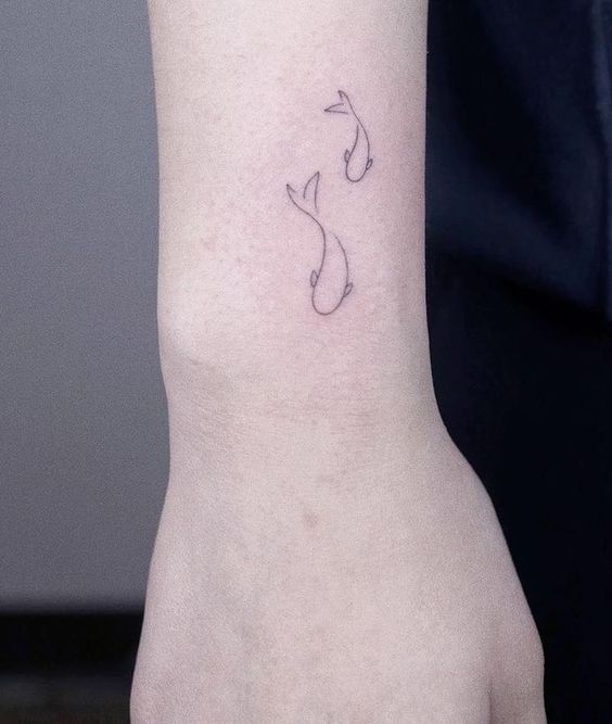 a person with a small tattoo on their left arm and wrist, showing the outline of a fish