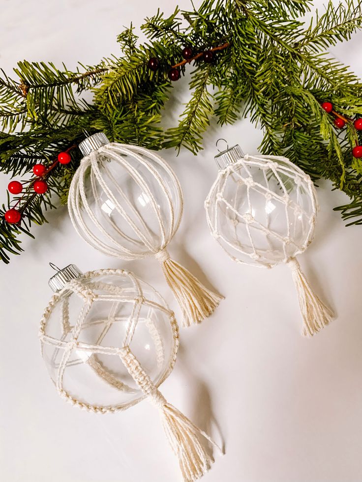 two glass ornaments are sitting on a table next to christmas greenery and red berries