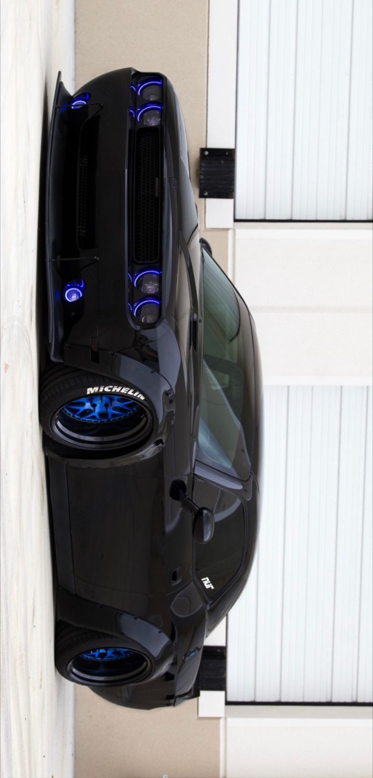 an aerial view of a black sports car parked in front of a garage door with its lights on