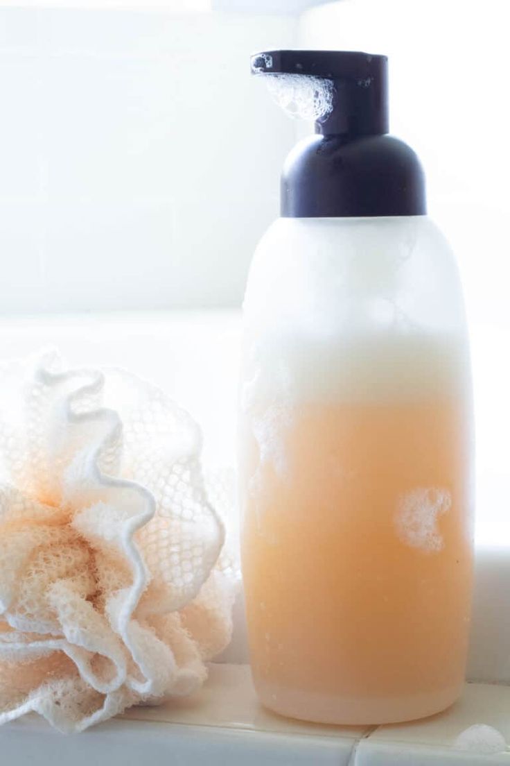 a bottle of soap sitting on top of a bathtub next to a towel and sponge