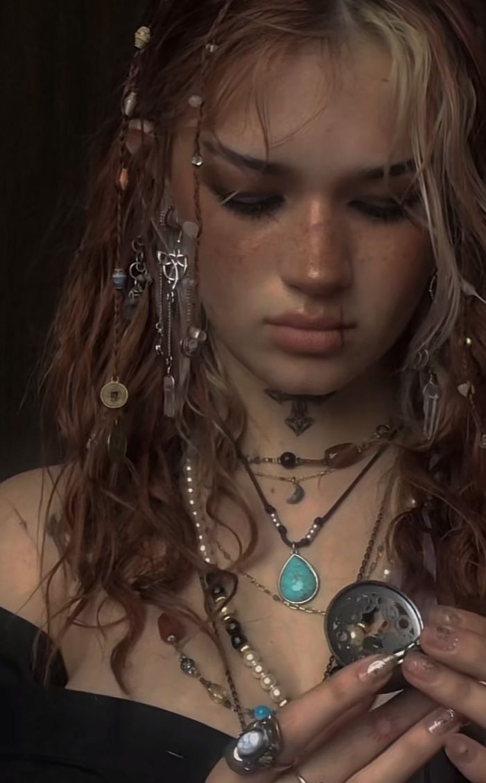 a woman with long hair and jewelry around her neck looking down at her cell phone