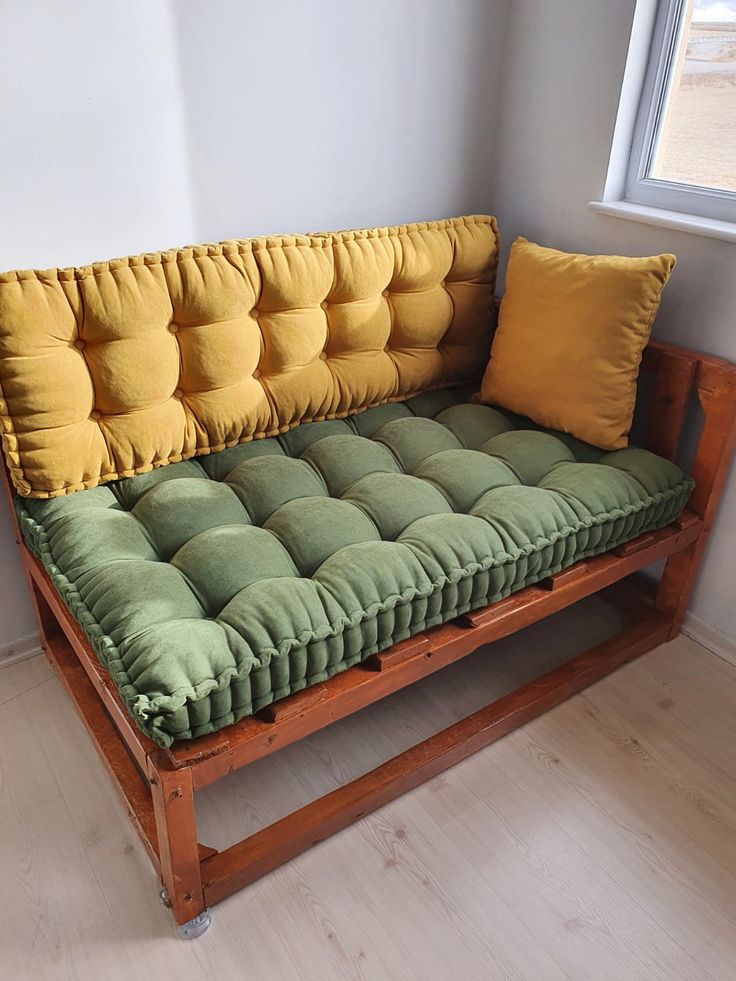 a green and yellow futon couch sitting on top of a hard wood floor next to a window