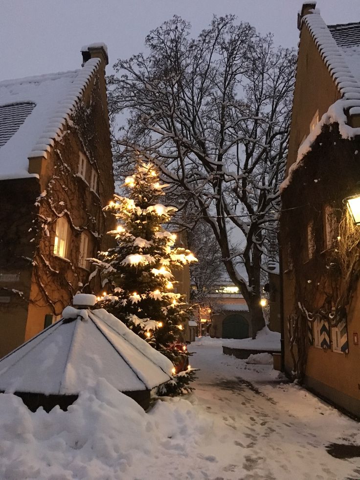 a snow covered street lined with buildings and a lit christmas tree in the foreground