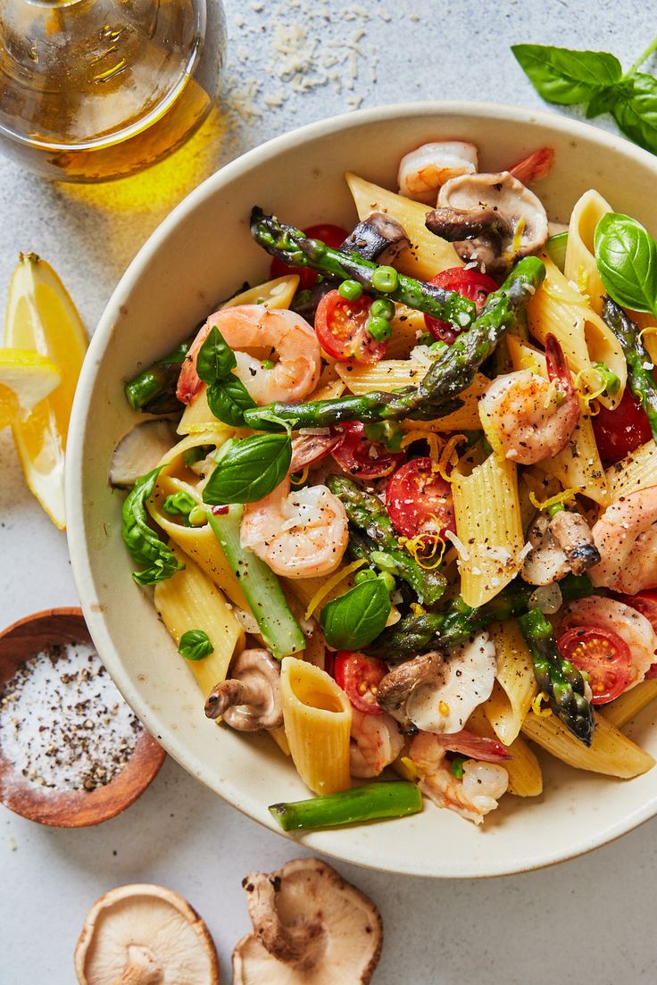 a white bowl filled with pasta, shrimp and asparagus on top of a table